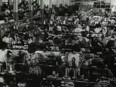 Workers operating textile sewing machines in a large factory floor.