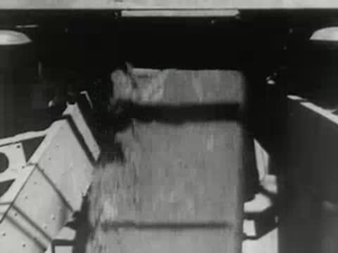 Bulk material pours from a chute into a ship; harbor view.