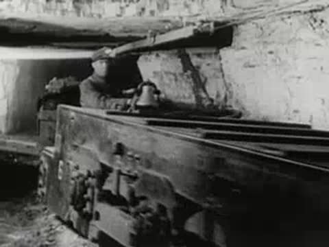 Mining cart loaded with dark material emerges from an underground tunnel.