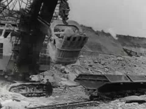 Large mechanical shovel loads dirt into a railway car in a quarry.