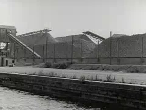 Material pours continuously from a chute into a storage facility near water.