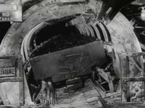 Crane unloads materials at industrial site near blast furnaces, 1950s documentary footage.