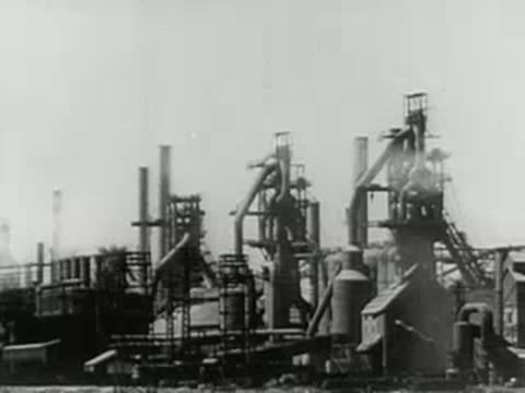 Exterior view of large industrial blast furnaces smoking at steel mill, 1950s.