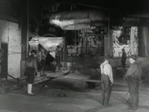 Group of workers stands inside industrial facility observing steel manufacturing, 1950s.