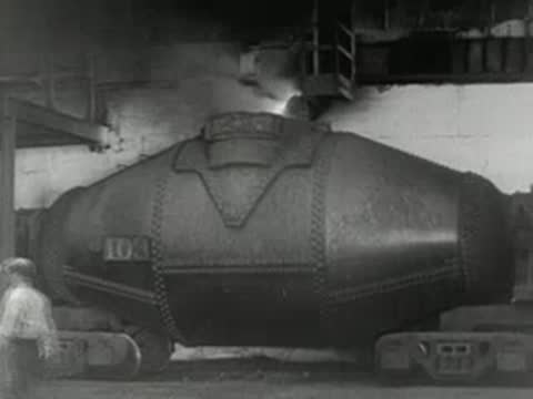 Large industrial torpedo car container sits on railway tracks inside factory, 1950s.