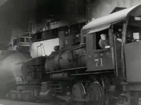 Industrial steam locomotive with driver in cab moves inside steel plant, 1950s.
