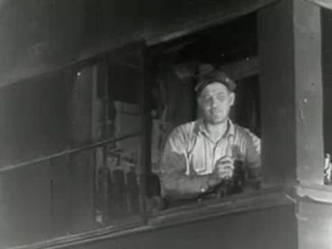 Worker looks out from control room window inside industrial plant, 1950s.