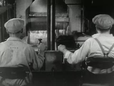 Workers operate machinery as glowing metal slabs move on conveyor belt, 1950s.