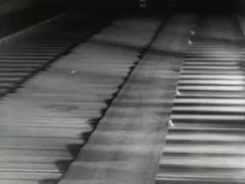 Hot metal slab is processed through heavy rolling mill machinery, 1950s.