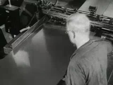 Worker guides continuous metal strip through industrial processing machinery, 1950s.