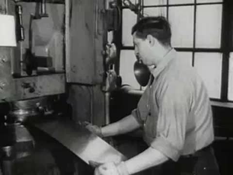 factory worker feeding metal sheet into industrial stamping machine, 1950s style