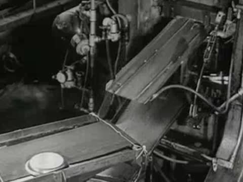 automated conveyor belt transporting stamped metal pan lids in factory, 1950s
