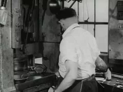 factory worker operating industrial press machine on metal parts, 1950s