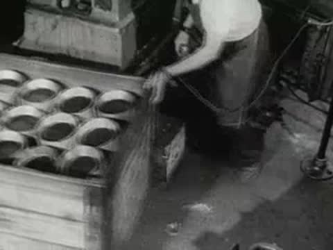 factory worker loading metal pan lids into wooden shipping crate, 1950s