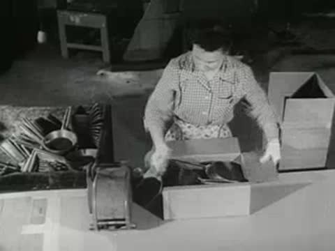 factory worker packing finished metal pans into cardboard shipping box, 1950s