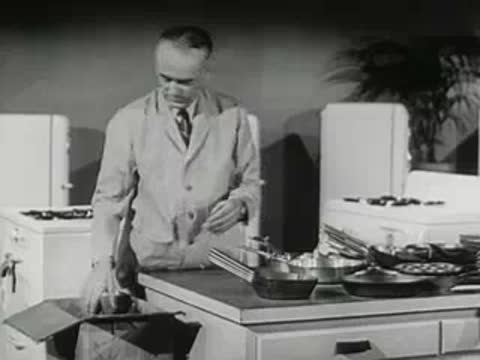 hardware store clerk unpacking box of metal pans on counter, 1950s