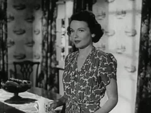 A woman in a floral dress stands in a domestic interior smiling.