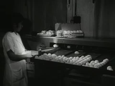 A worker operating an egg grading and packaging machine in a dim room