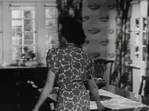 A woman walks across a room towards a window in a house.