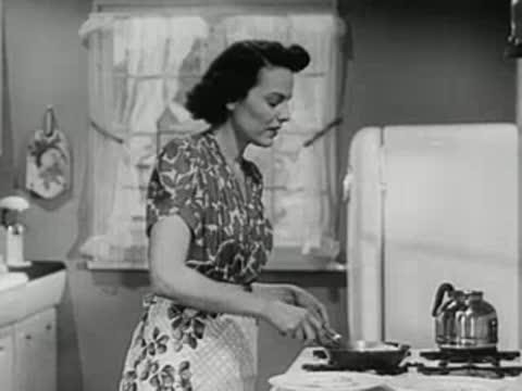 A woman cooking eggs in a pan on a gas stove in her kitchen