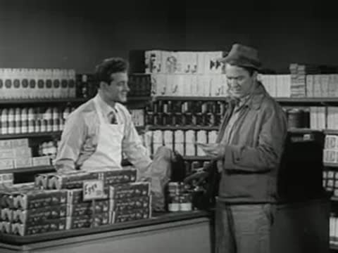 A grocery store clerk interacting with a customer at the checkout counter