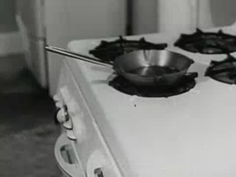 A woman stands in a kitchen next to a stove; pan; open-pit mine.