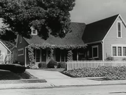 A suburban house exterior and a vintage car driving past on the street