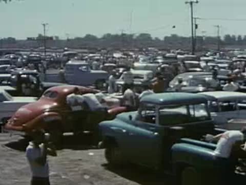Crowded parking lot with vintage cars and spectators at a race event.