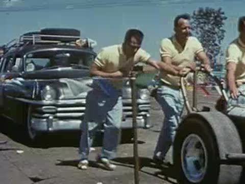 Men pushing a dragster car near the starting line under a banner.