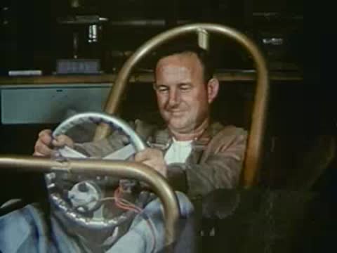 Driver sitting in a dragster cockpit and mechanics working on an engine.