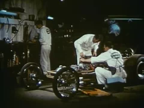 Mechanics working on the chassis of a dragster in a shop.