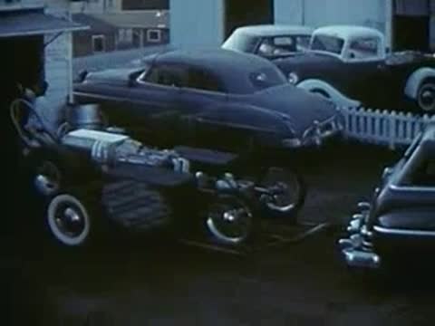 Welder working with sparks, dragster trailer, and car driving on street.