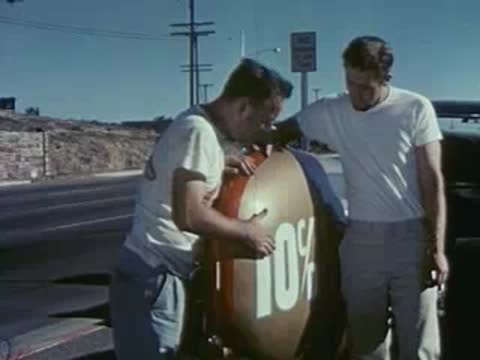 Two men stand by a round fuel tank marked 10% outdoors.