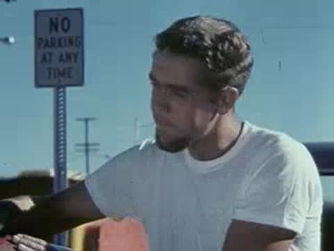 A man in a white t-shirt looks down near a vehicle component.