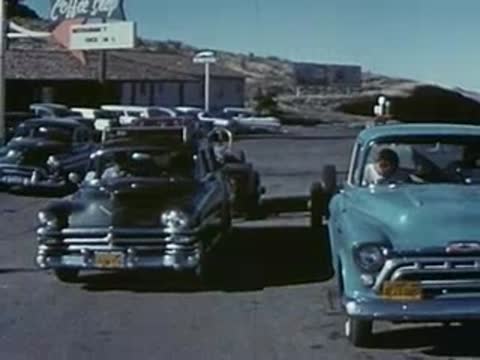 Cars drive along a winding road through a mountainous desert landscape.