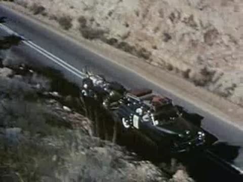 A blue car and a dark car drive along a winding desert road.