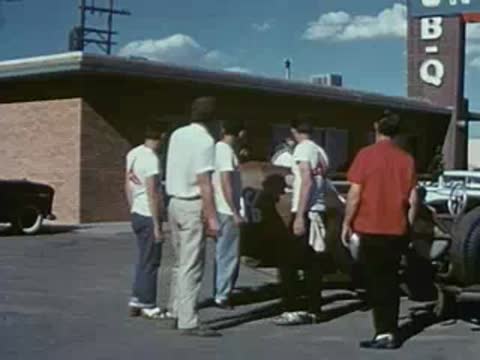 A group of men stand and converse near a race car outdoors.
