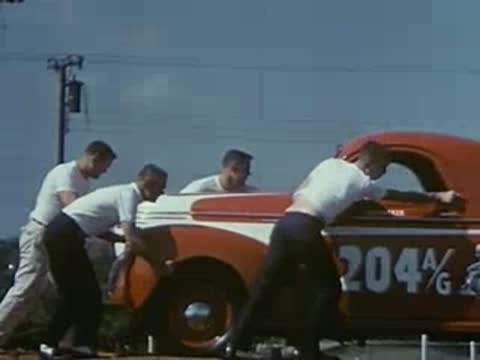 Crew members push a red race car toward a transport truck.