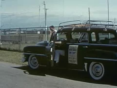 A man steps out of a vintage station wagon parked outdoors.