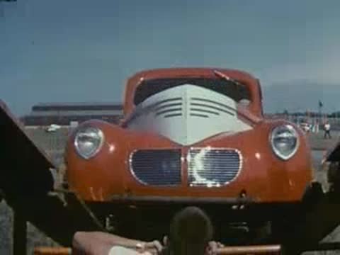 A red race car is viewed from below as it loads onto a transport truck.