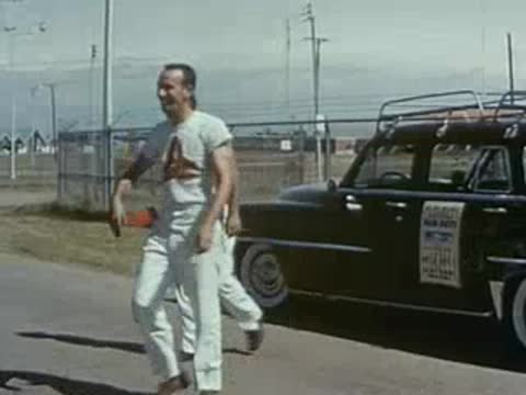 Two men walk past a parked vintage station wagon outdoors.