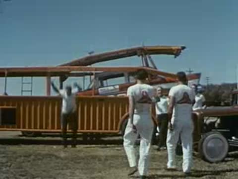 Men stand near a large orange transport truck in an open lot.