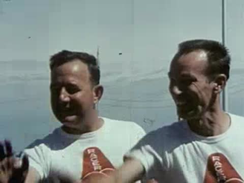Three men smile and gesture happily while standing together outdoors.