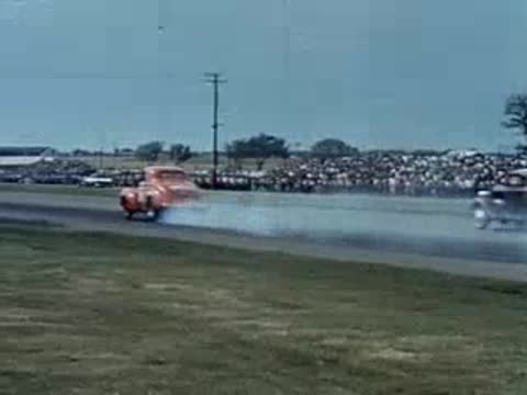 A woman films drag racing cars speeding down the track with a camera.