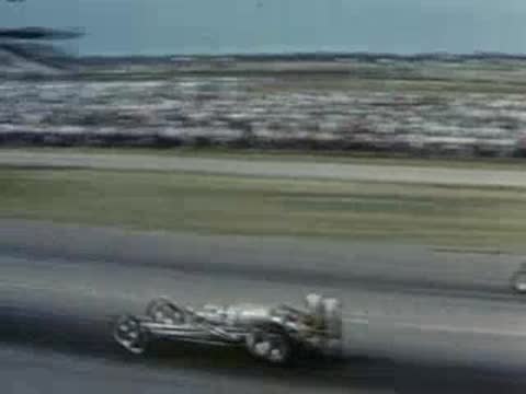 Two drag racers compete side by side on a track before a crowd.