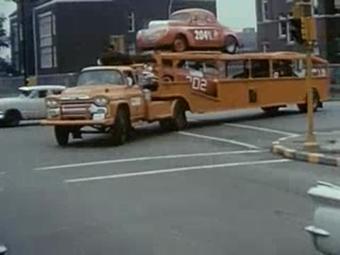 car carrier truck transporting vehicles on city street, 1950s