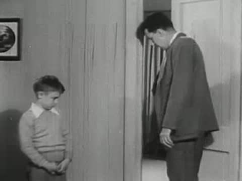 Father guiding crying young boy out of room.