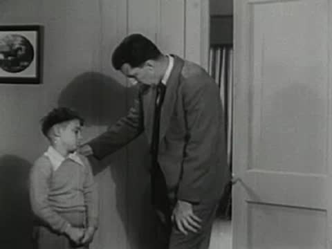 Father talking to sad young boy standing in hallway.