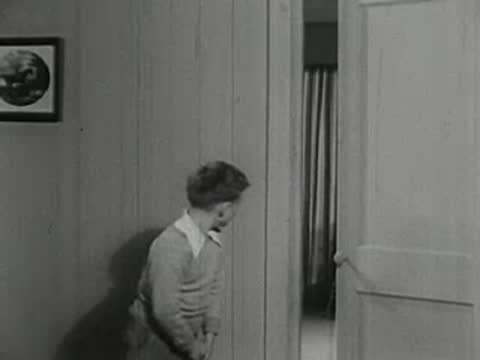 Young boy standing alone in hallway looking down.