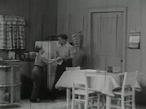 Two boys talking in kitchen with woman standing nearby.